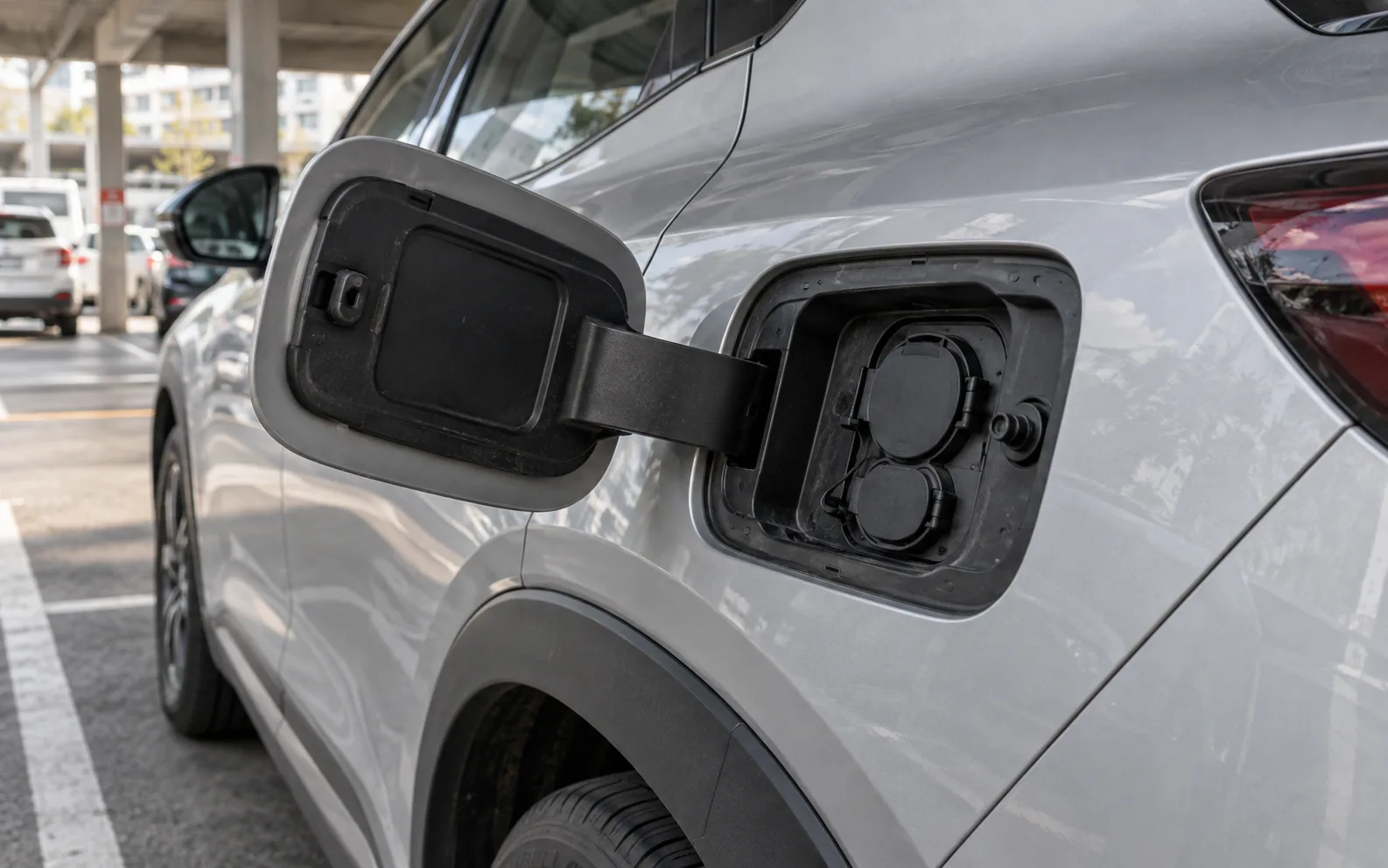 Geöffnete Ladeklappe eines silbernen Elektroautos mit geschlossenen Anschlusskappen